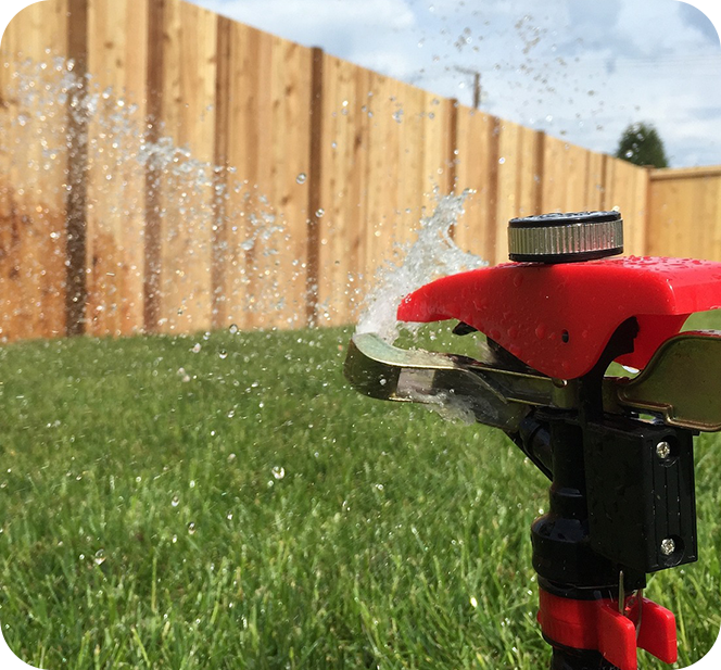 A red lawn sprinkler spraying water on the grass.